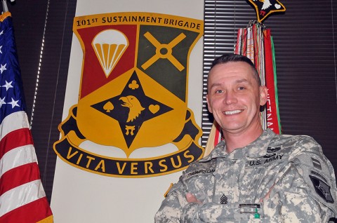 Command Sgt. Maj. David Thompson, command sergeant major of the 101st Sustainment Brigade, stands proudly next to the Designated Unit Insignia he created for the brigade. (Photo by Sgt. 1st Class Peter Mayes)