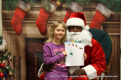 A young girl presents her Christmas drawing to Santa Claus
