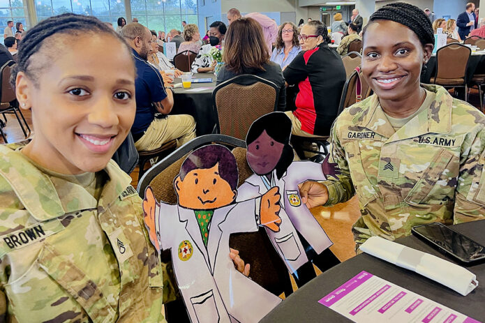 Blanchfield Army Community Hospital Partners in Education representatives Sgt. Ashley Gardner and Staff Sgt. Sierra Brown display paper dolls used to teach students about health, wellness and careers in healthcare. The Soldiers were attending the annual Clarksville-Montgomery County Education Foundation and Clarksville Area Chamber of Commerce Partners in Education Appreciation Breakfast in Clarksville, Tennessee, Aug. 30th. (Maria Yager)